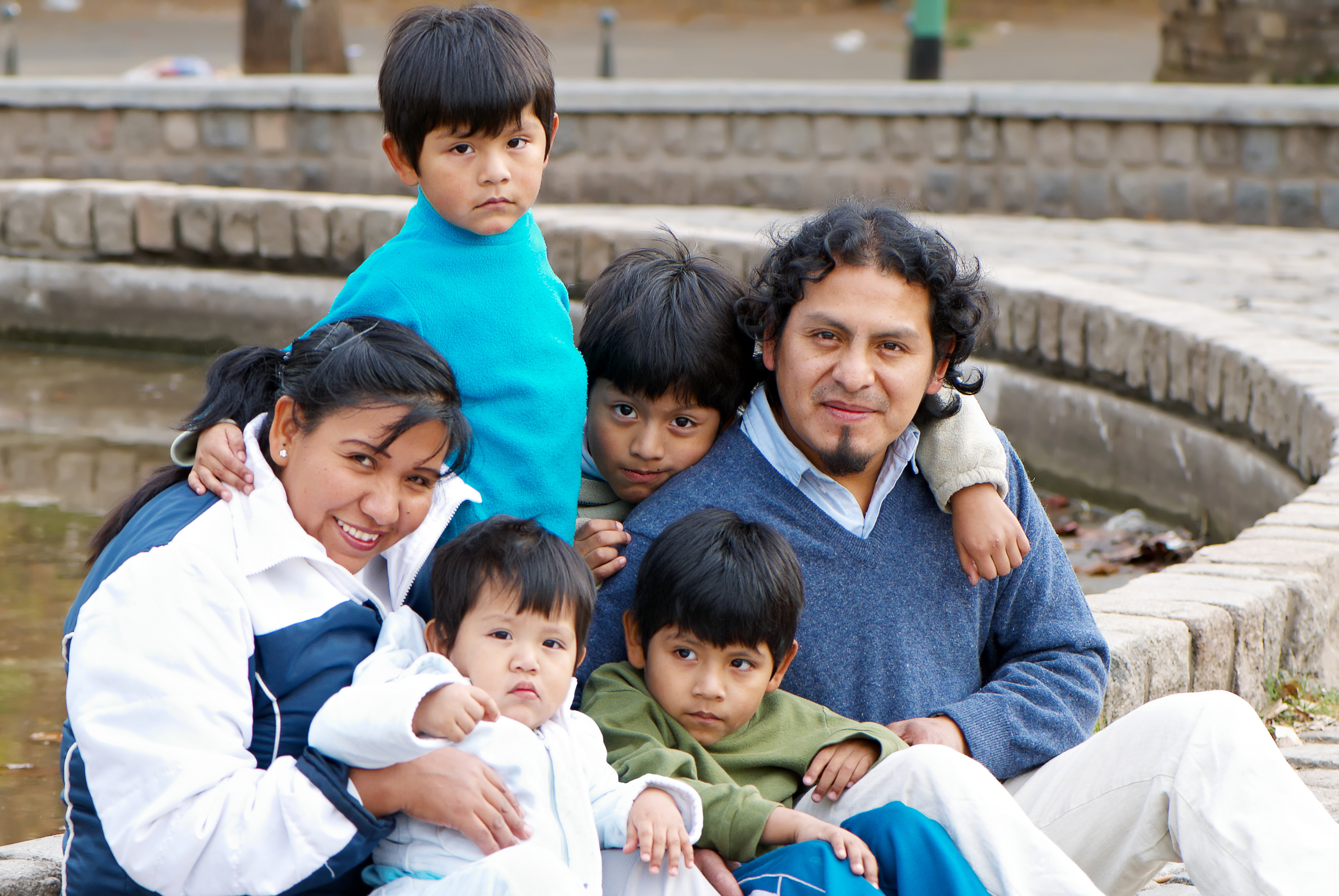 Latino family is sitting outside by a fountain.